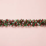 Shiny red and green tinsel garland dotted with white snowflakes stretches horizontally across a pale pink background.