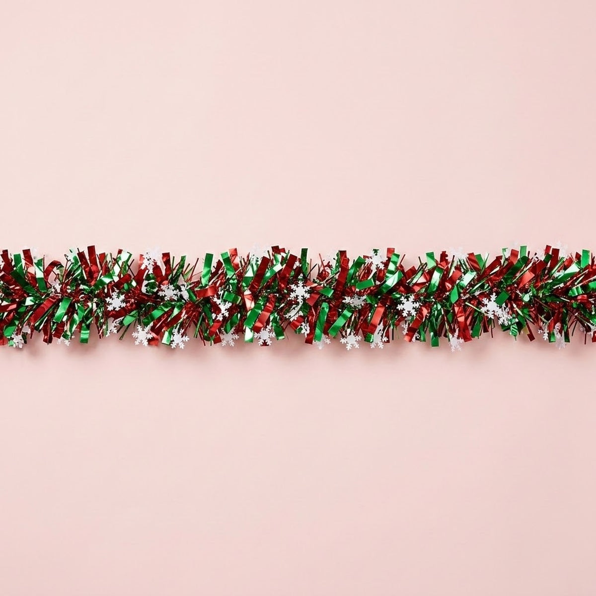 Shiny red and green tinsel garland dotted with white snowflakes stretches horizontally across a pale pink background.