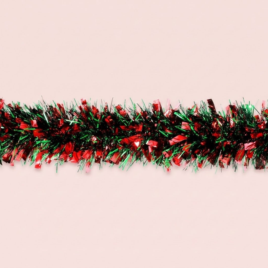 Red and green tinsel garland with wide reflective strips runs horizontally across a pale pink background.
