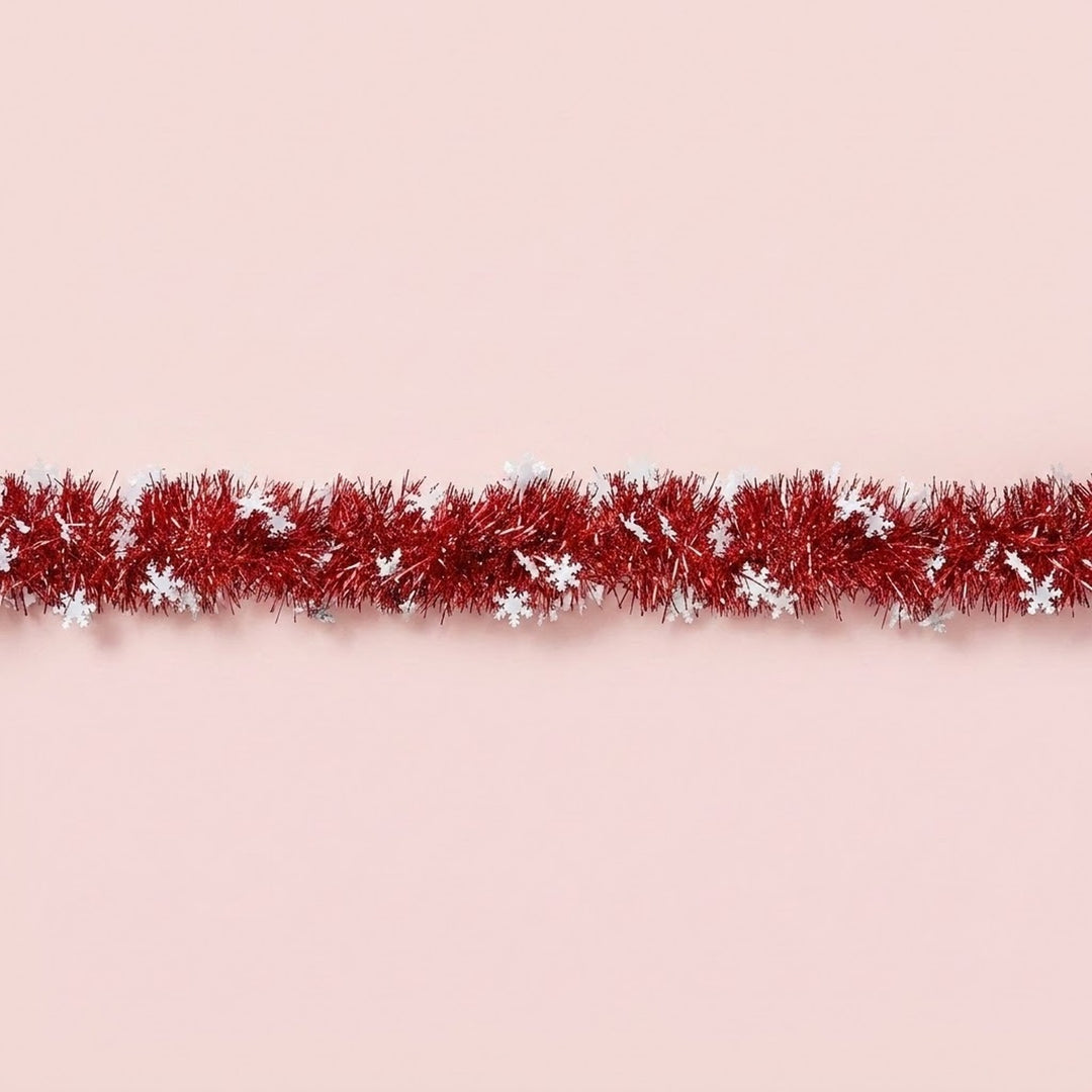 Red tinsel garland decorated with white snowflakes runs horizontally across a pale pink background.