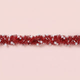 Red tinsel garland decorated with white snowflakes runs horizontally across a pale pink background.