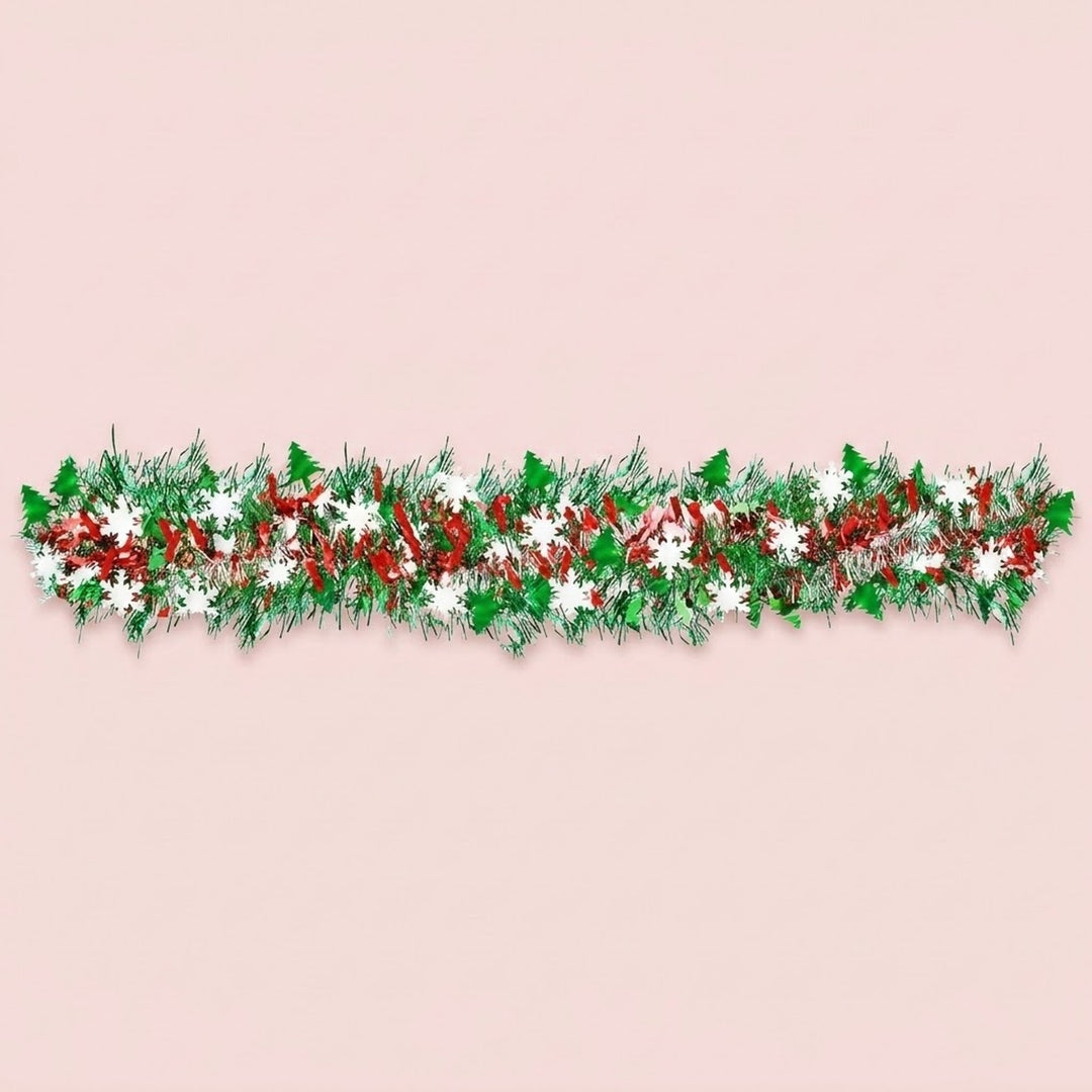 Green, red, and silver tinsel garland with green tree shapes and white snowflakes stretches horizontally across a pale pink background.