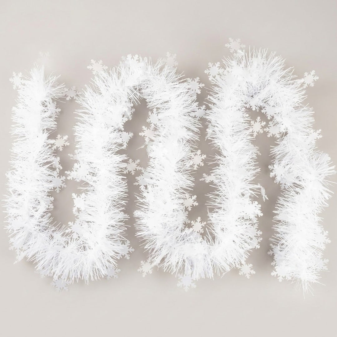 White tinsel garland decorated with white snowflakes forms loose loops on a light gray background.