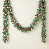 Green and red tinsel garland with white snowflakes and green tree cutouts hangs in a swag against a cream background.