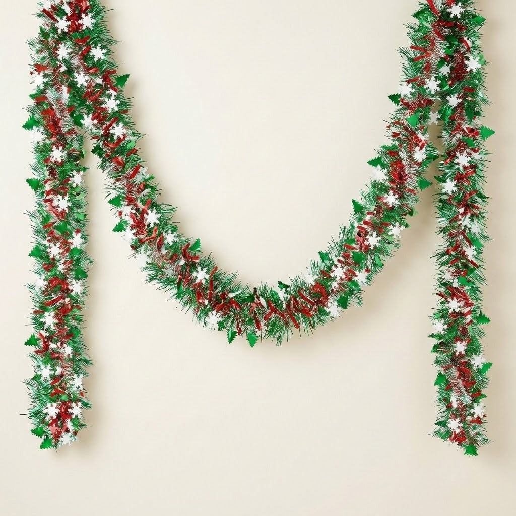 Green and red tinsel garland with white snowflakes and green tree cutouts hangs in a swag against a cream background.