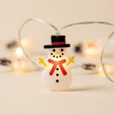 String light with glowing white snowmen, black hats, red scarves, and yellow arms on clear wiring against a cream background.