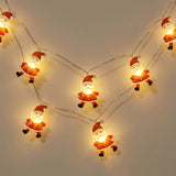 Red and white Santa string lights glow warm yellow along looping silver wires against a beige wall.