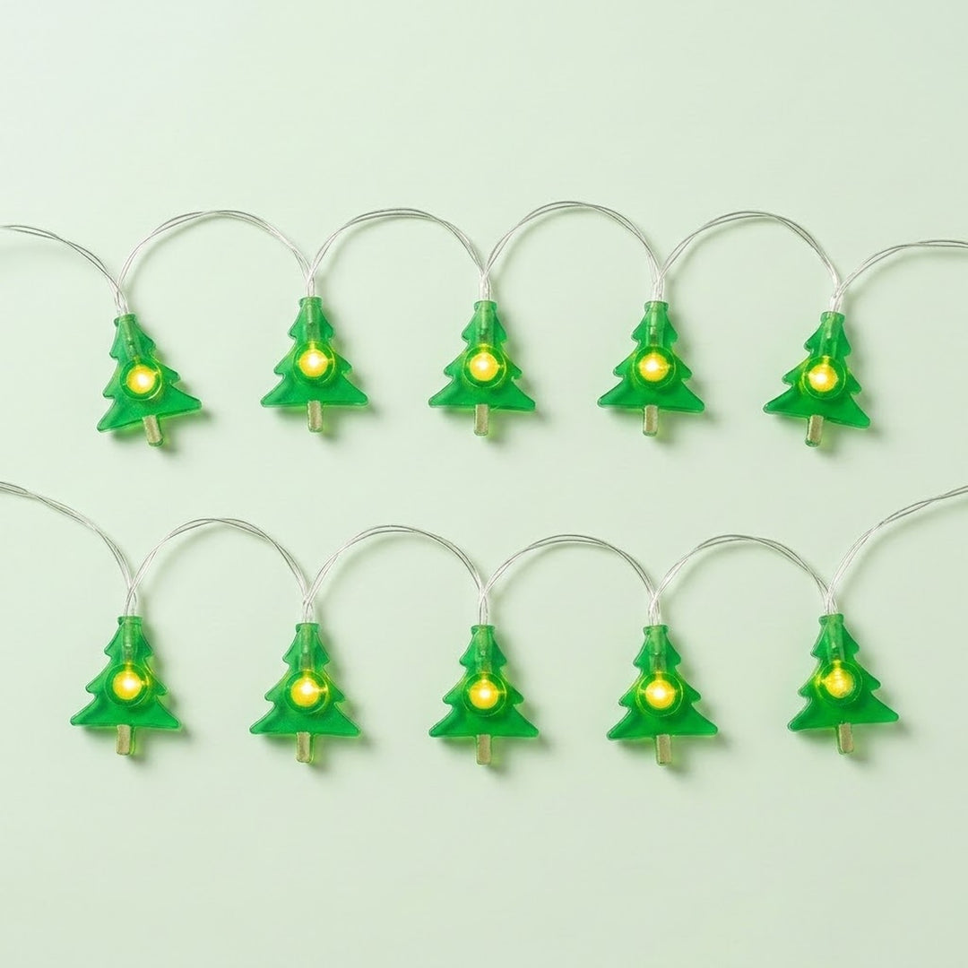 Green Christmas tree string lights with glowing yellow centers and silver wires form two rows against a pale green background.