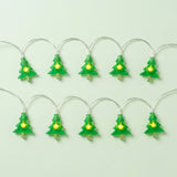 Green Christmas tree string lights with glowing yellow centers and silver wires form two rows against a pale green background.