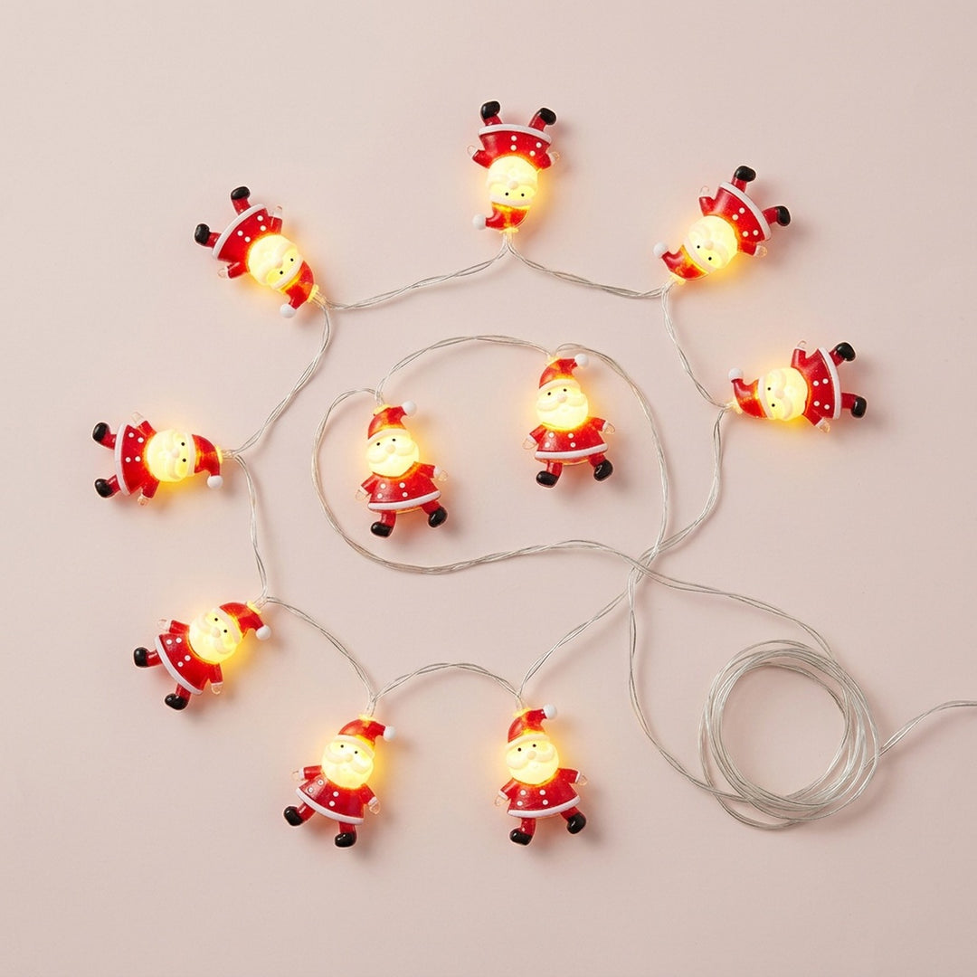 Red and white Santa string lights glow on a pale pink background beside a coiled length of silver wire.
