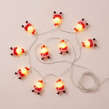 Red and white Santa string lights glow on a pale pink background beside a coiled length of silver wire.