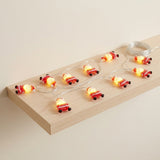 Glowing red Santa string lights lie across a pale wooden floating shelf, with clear wire coiled at one end.