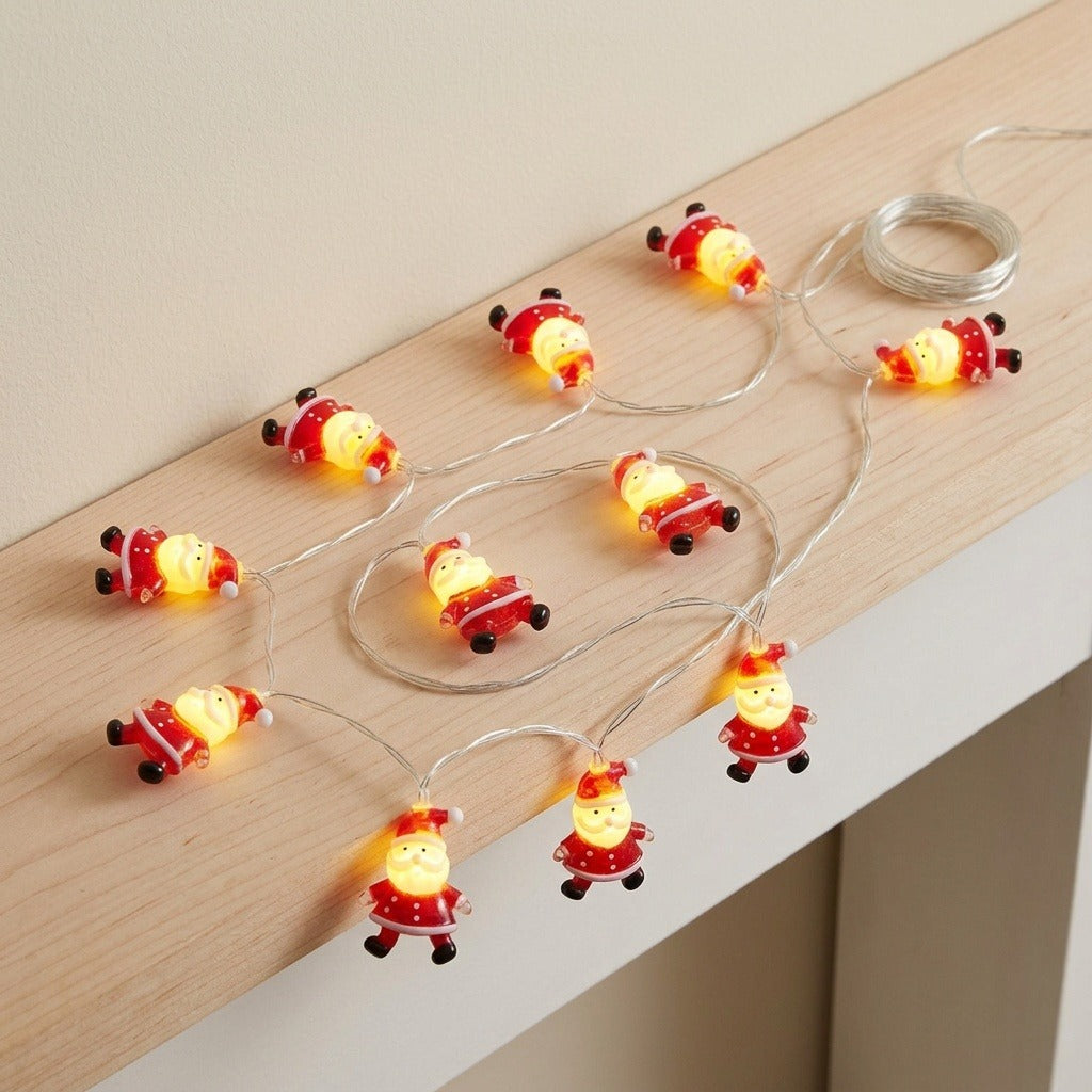 Red Santa string lights glow along a pale wooden ledge, with three figures hanging over the edge and wire coiled above.