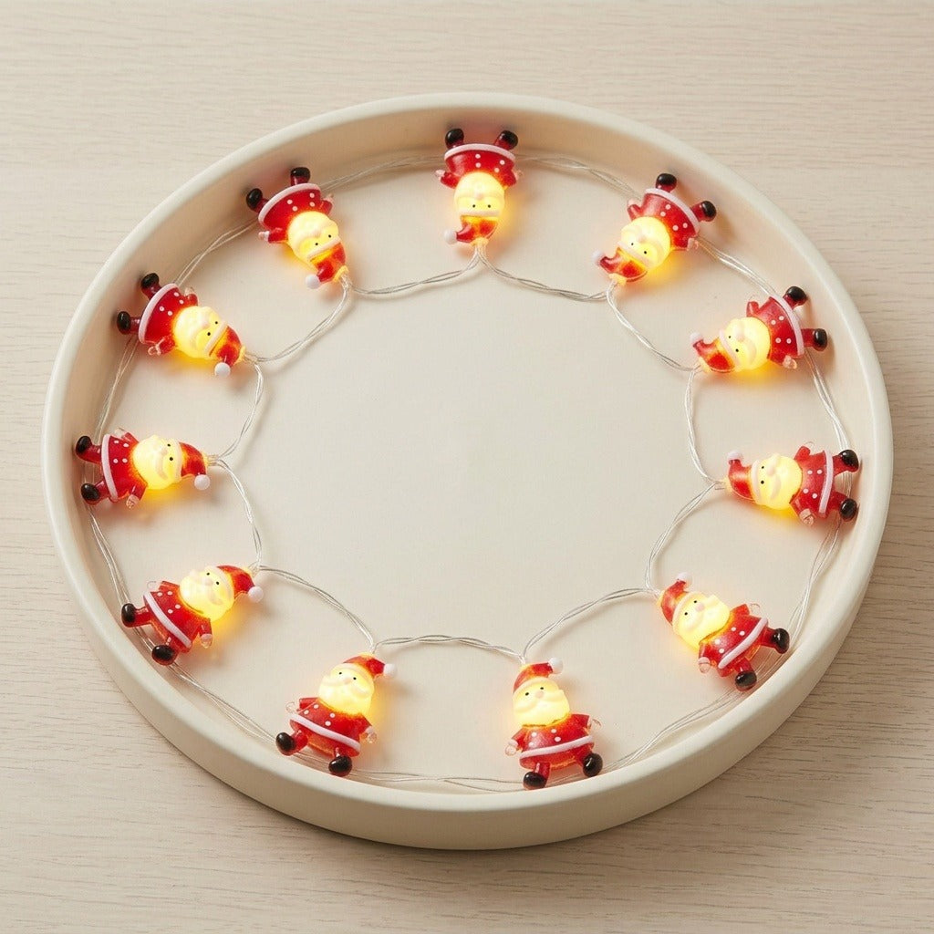 Glowing red and white Santa string lights form a circle inside a round cream tray on a pale wooden surface.