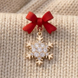 A red bow earring with a clear-studded gold-tone snowflake drop rests on cream knitted fabric.