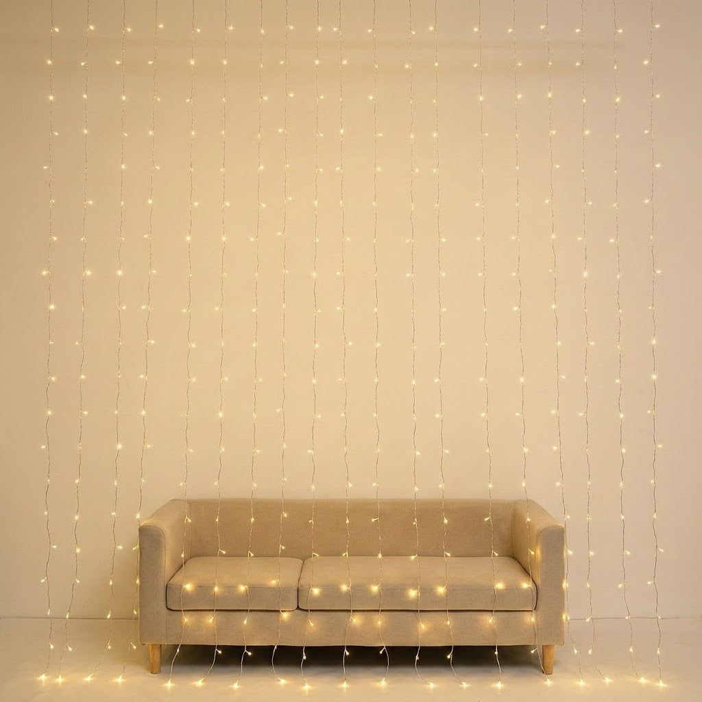 Warm white curtain lights hang in front of a beige sofa against a cream wall.