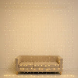 Warm white curtain lights hang in front of a beige sofa against a cream wall.