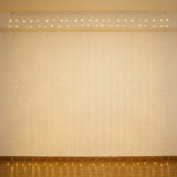 Warm white curtain lights hang against a cream wall above a brown baseboard, reflecting on the wooden floor.