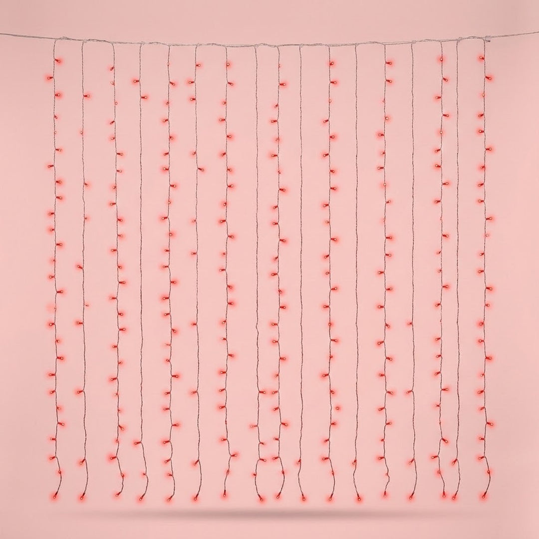 Red curtain string lights hang in vertical strands from a horizontal wire against a pale pink background.