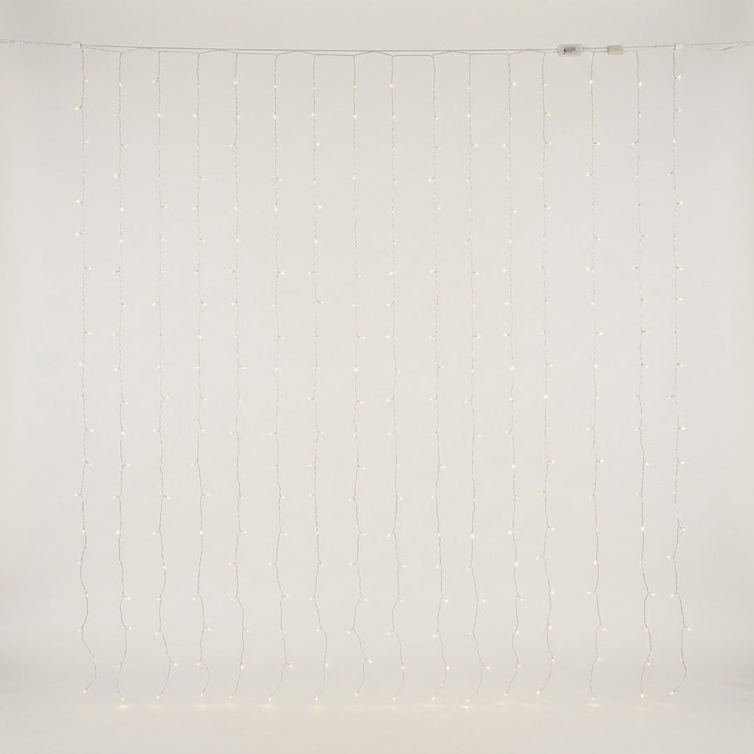 Warm white curtain lights hang in vertical strands against an off-white background, with connectors visible along the top cable.