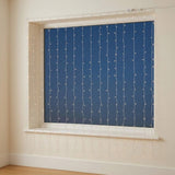 White curtain lights hang across a white-framed window with a dark blue view outside and wooden flooring below.