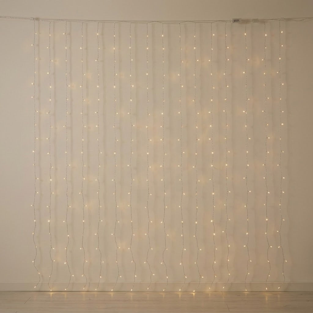 Warm white curtain lights hang in vertical strands against a bare cream wall above a pale wooden floor.