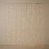 Warm white curtain lights hang in vertical strands against a bare cream wall above a pale wooden floor.