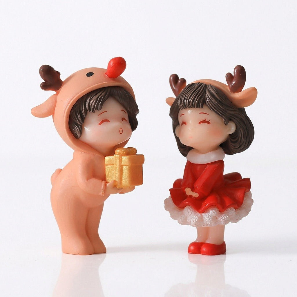 Two plastic Christmas figurines with antlers, a peach outfit, red dress, and gold gift stand against a white background.