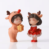 Two plastic Christmas figurines with antlers, a peach outfit, red dress, and gold gift stand against a white background.