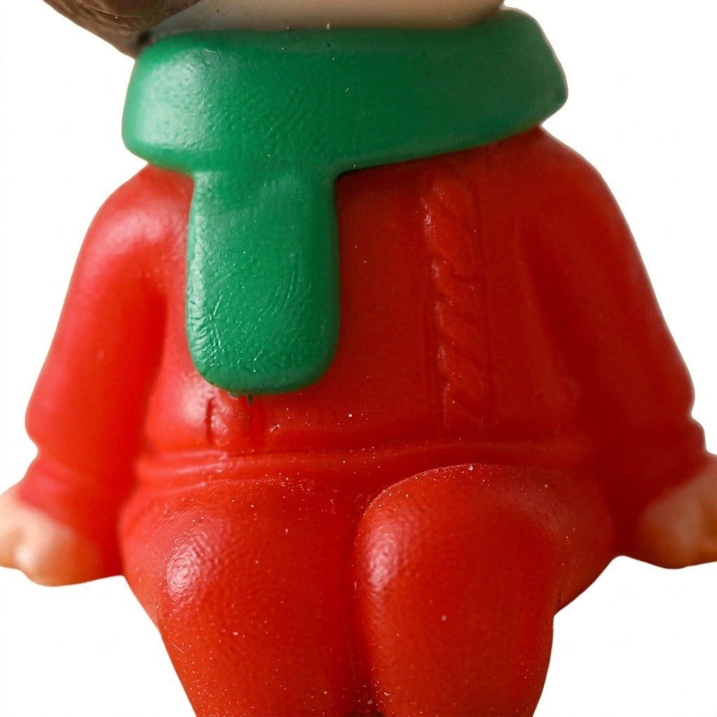 A close-up of a plastic Christmas figurine shows textured red clothing and a green scarf against a white background.