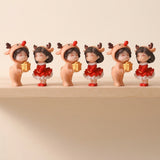 Three pairs of plastic Christmas figurines in peach reindeer outfits and red dresses stand along a wooden shelf against a beige background.