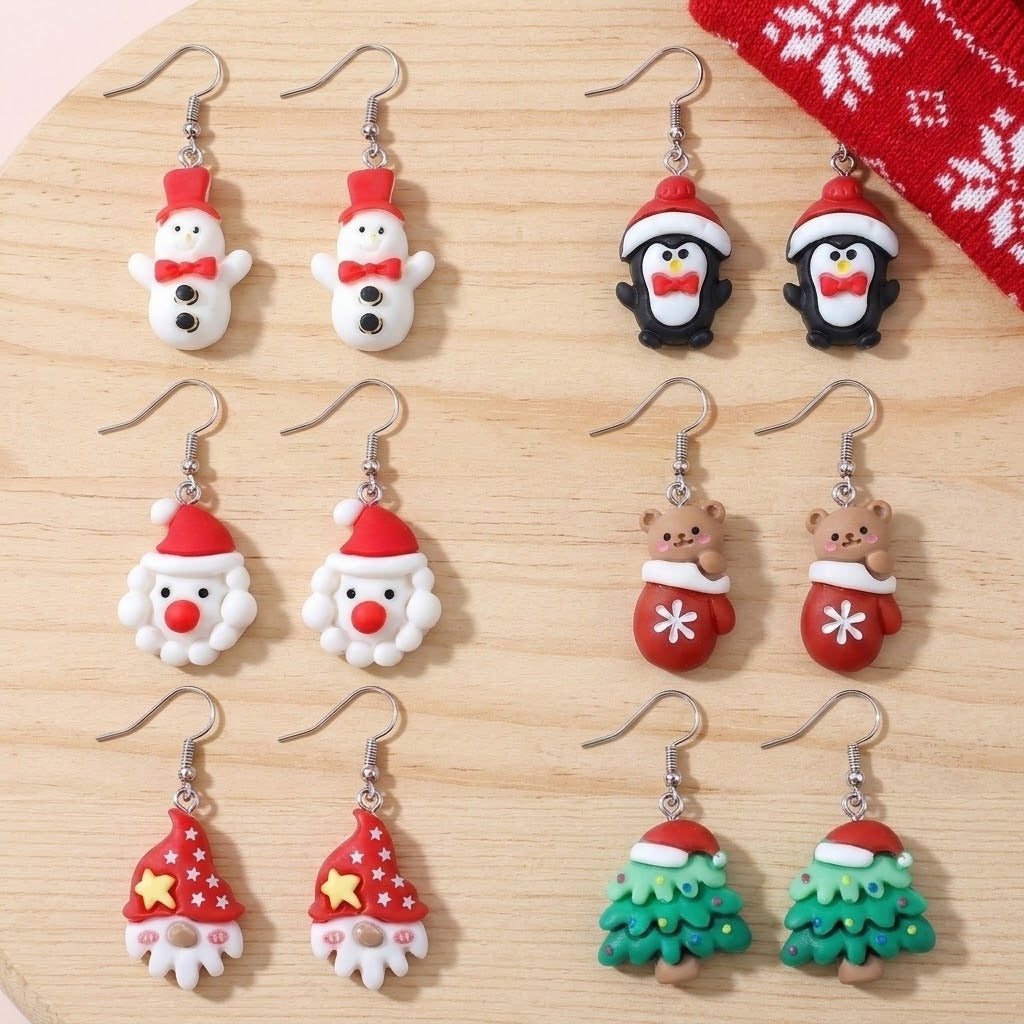 Six pairs of colorful Christmas drop earrings with silver hooks, including snowmen, penguins, Santas, and trees, arranged on light wood.