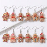 Twelve gingerbread person drop earrings with silver hooks, red bows, hats, and buttons arranged in two rows on a white stepped background.