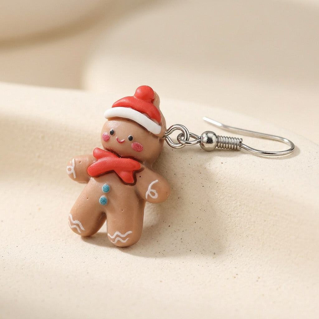 Close-up of a tan gingerbread person drop earring with red hat and bow, turquoise buttons, and a silver hook on cream surface.