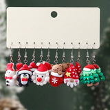 A set of colorful Christmas drop earrings with silver hooks hangs from a blank cream display card against a dark green background.