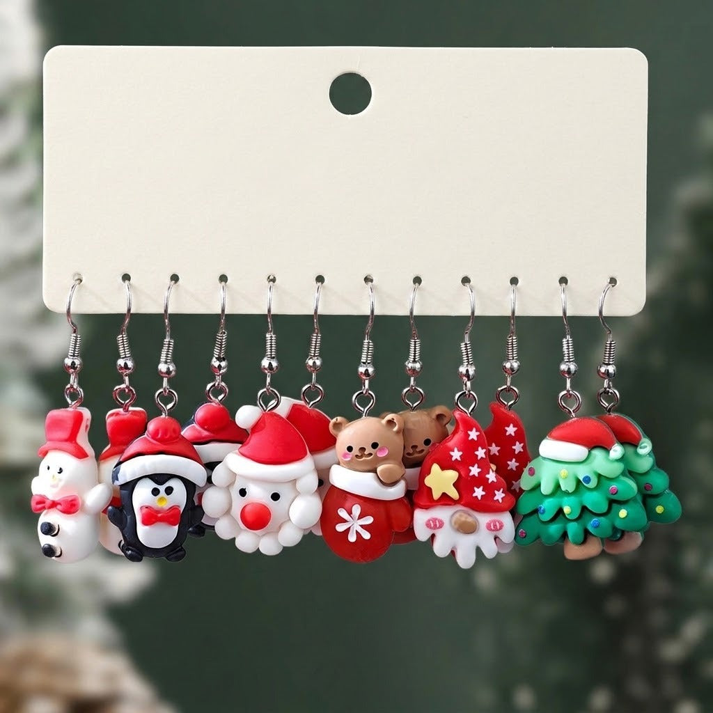 A set of colorful Christmas drop earrings with silver hooks hangs from a blank cream display card against a dark green background.