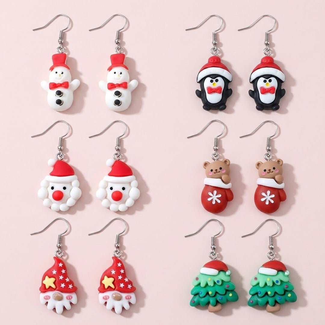 Six pairs of Christmas-character drop earrings with silver hooks show snowmen, penguins, Santa, a mitten bear, gnomes, and trees on a pale pink background.