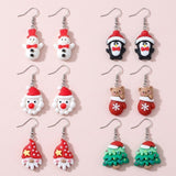 Six pairs of Christmas-character drop earrings with silver hooks show snowmen, penguins, Santa, a mitten bear, gnomes, and trees on a pale pink background.