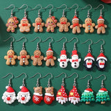 Christmas drop earrings with silver hooks, including gingerbread figures, penguins, Santas, and trees, arranged in three rows on dark green fabric.