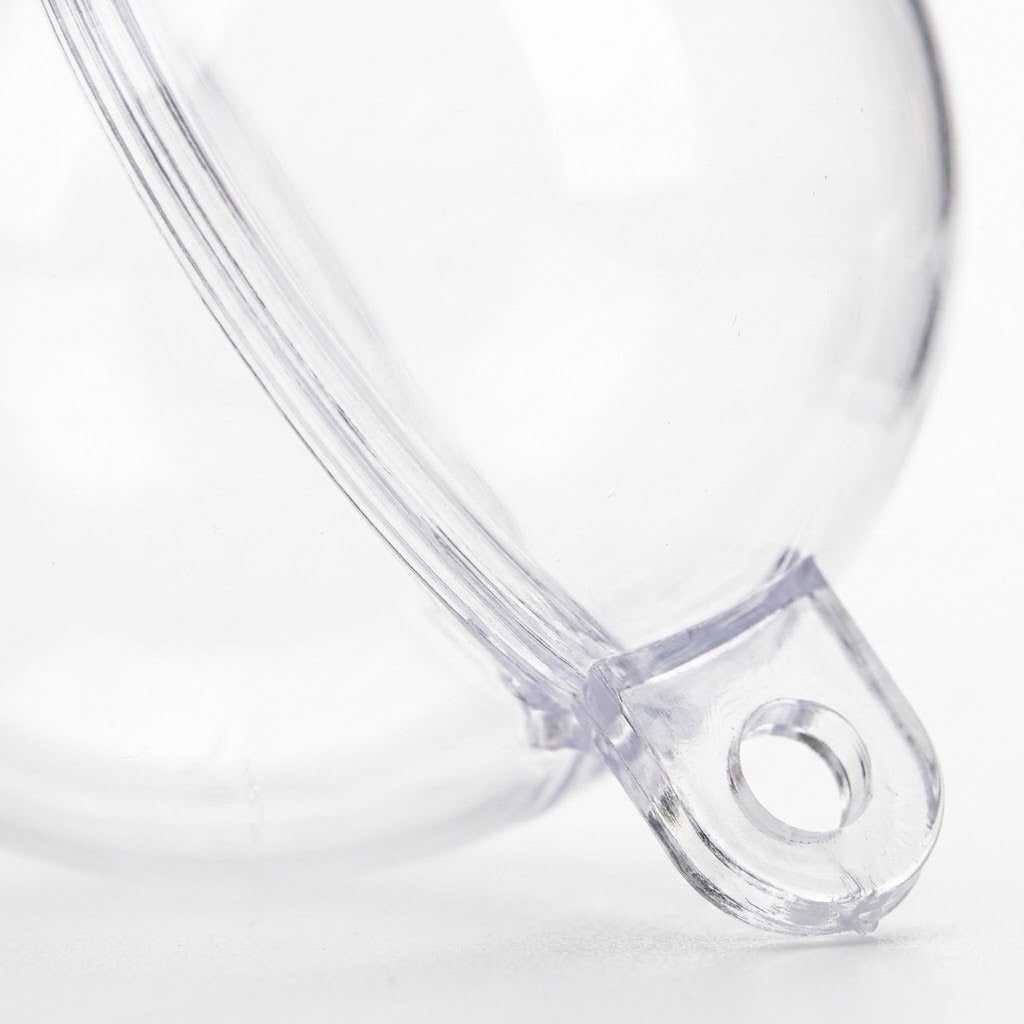 A clear plastic fillable ornament appears close up against white, showing its curved joining edge and hanging tab with a circular hole.