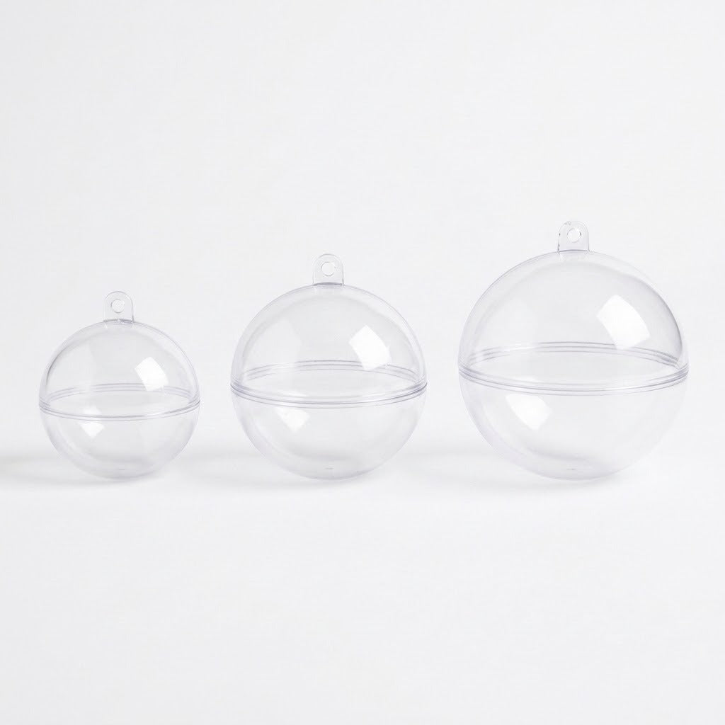 Three empty clear plastic fillable ornaments in increasing sizes stand on a white background, showing joining seams and hanging tabs.
