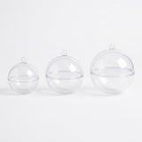 Three empty clear plastic fillable ornaments in increasing sizes stand on a white background, showing joining seams and hanging tabs.