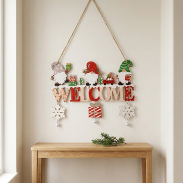 Wooden Christmas ornament with red and natural WELCOME letters, three gnomes, snowflakes, and bells hangs above a console table.
