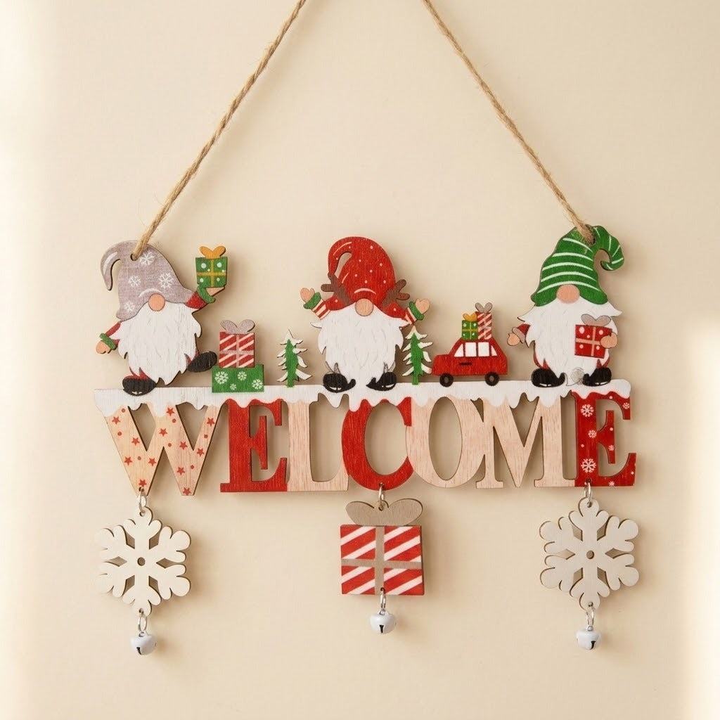 A festive wooden hanging wall decoration featuring four Christmas gnomes, a red car, gift boxes, and a large 'WELCOME' sign with snowflake ornaments below, suspended by twine against a plain beige wall.