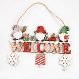 Wooden Christmas ornament with three colorful gnomes, WELCOME lettering, dangling snowflakes, a striped gift, and silver bells appears against white.
