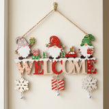 Wooden Christmas ornament with colorful gnomes, WELCOME letters, snowflakes, and bells hangs by twine from a brass-colored hook on a cream door.