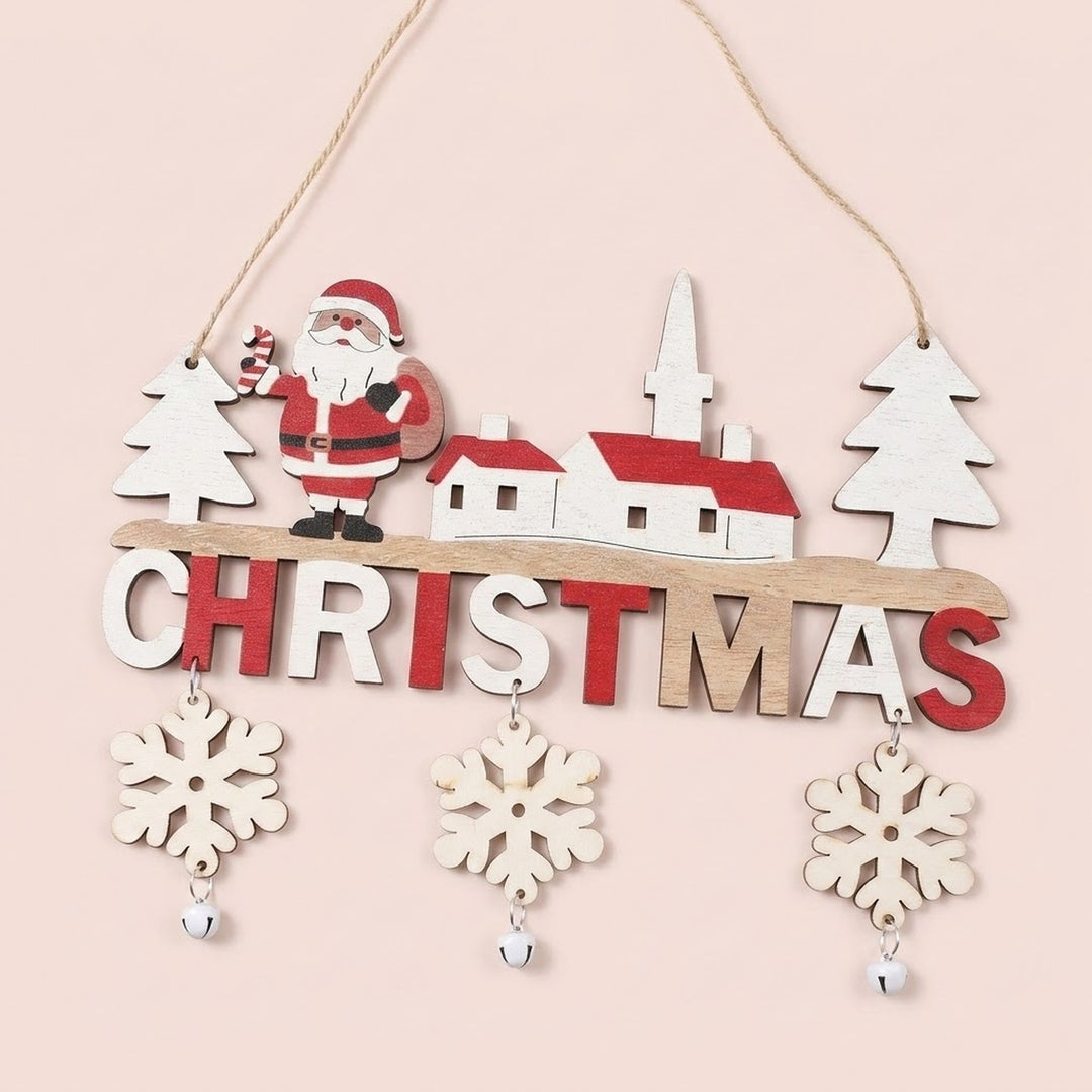 Wooden Christmas ornament featuring Santa, white village buildings with red roofs, dangling snowflakes, and silver bells hangs against a pale pink background.