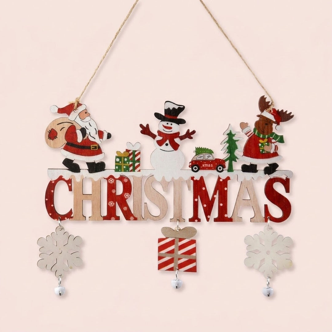 Wooden Christmas ornament with Santa, snowman, reindeer, red and natural lettering, dangling snowflakes, a striped gift, and bells hangs against pale pink.