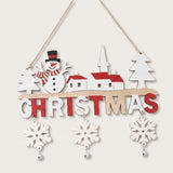 Wooden Christmas ornament featuring a snowman, white village buildings with red roofs, dangling snowflakes, and silver bells hangs against an off-white background.
