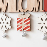 Wooden Christmas ornament detail shows white snowflakes and a red striped gift dangling above silver bells against a white background.